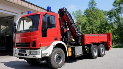 Roter Feuerwehr-Lkw mit Kran und Hebebühne vor einer Halle
