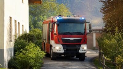 Rotes Feuerwehrfahrzeug mit Blaulicht fährt auf einer Straße in bergiger Landschaft