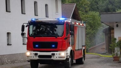 Rotes Feuerwehrfahrzeug mit blauem Blaulicht und gelbem Schlauch davor