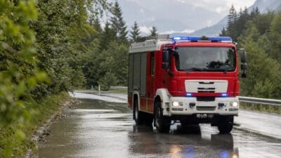 Rotes Feuerwehrfahrzeug mit Blaulicht auf nasser Straße in bergiger Landschaft