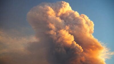 Eine große orange leuchtende Wolke türmt sich vor blauem Himmel auf.