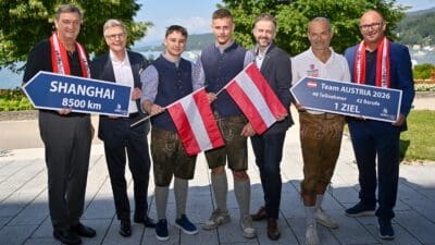 Männer in Tracht und Anzügen halten österreichische Flagge und Schilder am Seeufer