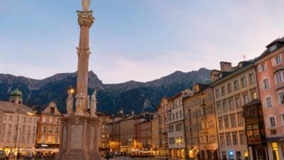 Hohe Steinsäule mit mehreren Statuen auf einem Platz in Innsbruck vor Bergkulisse bei Abenddämmerung