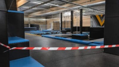 Leerer Trampolinpark mit blauen und schwarzen Matten sowie rot-weißem Warnband im Vordergrund