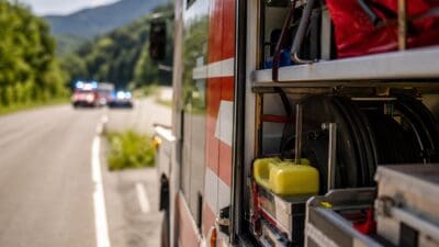 Offenes Abteil eines roten Feuerwehrfahrzeugs mit Schläuchen und gelben Behältern auf einer Landstraße