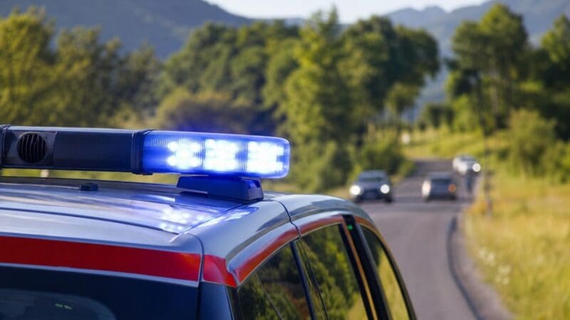 Blaues Blaulicht leuchtet auf dem Dach eines Polizeifahrzeugs auf einer Landstraße vor Bergen.