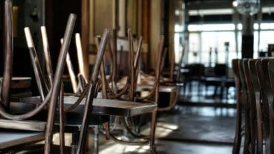 Umgestülpte Holzstühle stehen auf Tischen in einem leeren Gastronomiebetrieb