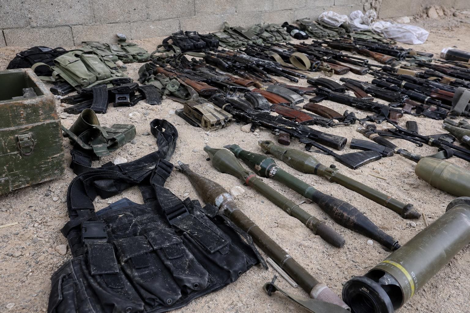 Zahlreiche Gewehre, Raketenwerfer und Munition liegen auf sandigem Boden ausgebreitet.