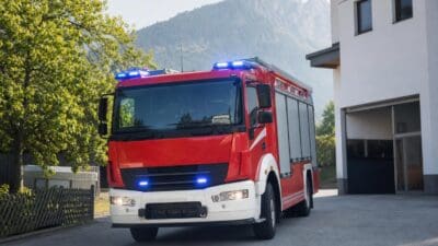 Rotes Feuerwehrfahrzeug mit blauen Blaulichtern vor einem Gebäude in bergiger Landschaft