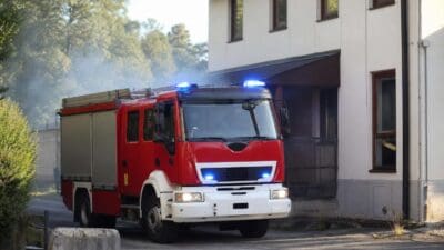 Rotes Feuerwehrfahrzeug mit leuchtenden blauen Blaulichtern vor einem Gebäude