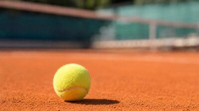 Ein gelber Tennisball liegt auf der Oberfläche eines roten Sandplatzes