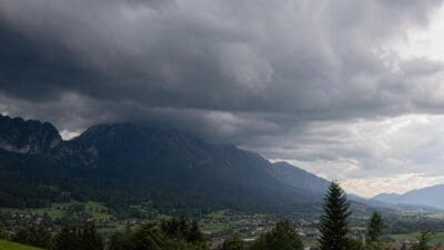 Dunkle Gewitterwolken hängen über Berglandschaft mit Tal und Ortschaft.