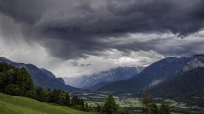 Dunkle Gewitterwolken über einem grünen Tal mit Bergen und Feldern