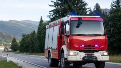 Rotes Feuerwehrfahrzeug mit Blaulicht auf einer Landstraße in bergiger Landschaft