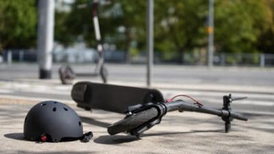 Ein schwarzer Helm liegt neben einem umgestürzten E-Scooter auf einem Gehweg.