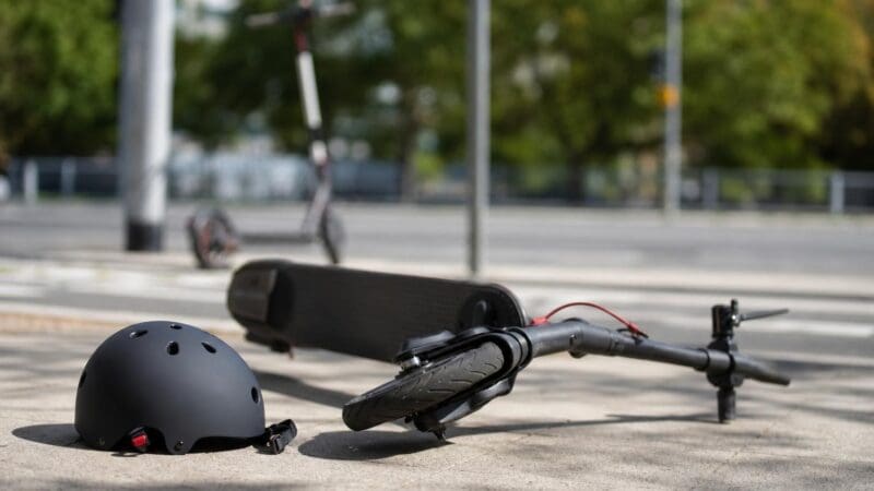 Ein schwarzer Helm liegt neben einem umgestürzten E-Scooter auf einem Gehweg.