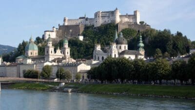 Die Festung Hohensalzburg thront über der Salzburger Altstadt mit grünen Kirchenkuppeln und dem Fluss Salzach.