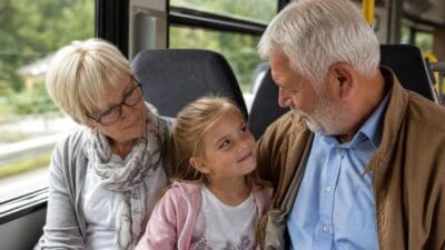 Ältere Frau und Mann mit jungem Mädchen sitzen eng beieinander in einem Bus.