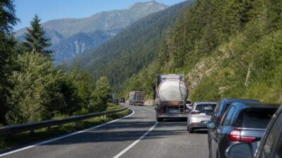 Fahrzeuge fahren auf einer kurvigen zweispurigen Straße durch ein bewaldetes Bergtal in Tirol.