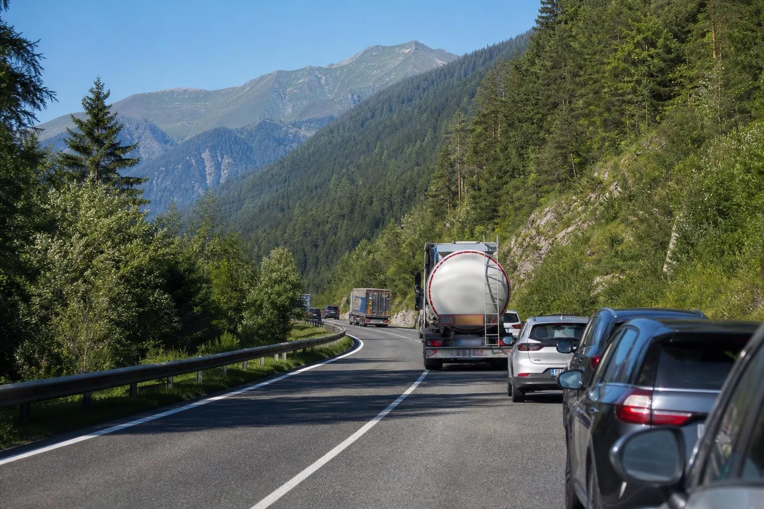 Fahrzeuge fahren auf einer kurvigen zweispurigen Straße durch ein bewaldetes Bergtal in Tirol.