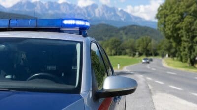 Graues Polizeiauto mit blauem Blaulicht auf dem Dach an einer Landstraße mit Bergpanorama im Hintergrund