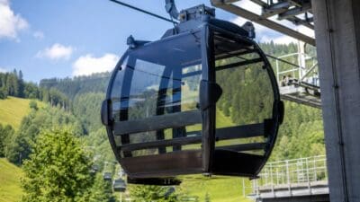 Schwarze Gondelkabine mit Glasfenstern hängt an der Seilbahn vor grünen Bergen