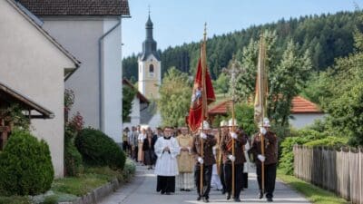 Geistliche und Feuerwehrleute tragen Fahnen und Kreuz bei einer Prozession in St. Martin