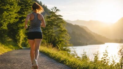 Eine Frau läuft von hinten gesehen auf einem Weg am Ufer eines Sees in den Bergen.