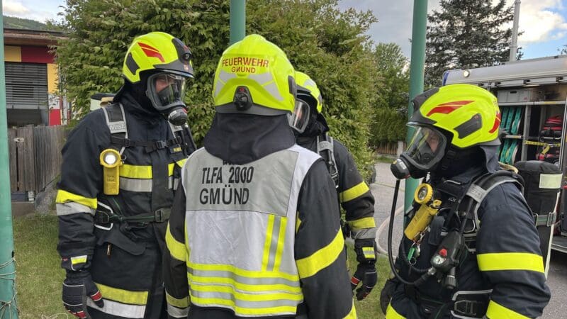 Mehrere Feuerwehrleute der Feuerwehr Gmünd in Schutzkleidung und Atemschutz stehen zusammen.