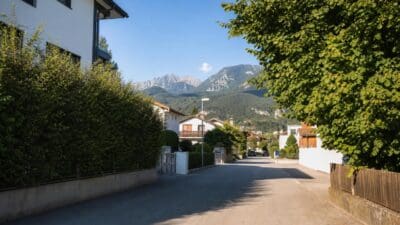 Sonnenbeschienene Straße in einem Wohngebiet mit Häusern Büschen und Bergen im Hintergrund