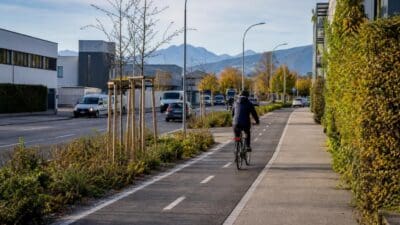 Radfahrer mit Helm fährt auf markiertem Radweg neben Straße, Gehweg und Bergen