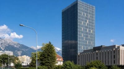 Hochhaus mit Glasfassade vor Bergpanorama unter blauem Himmel in Innsbruck