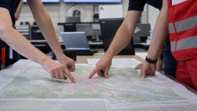 Mehrere Personen zeigen mit den Fingern auf eine große Karte auf einem Tisch in einem Einsatzraum.