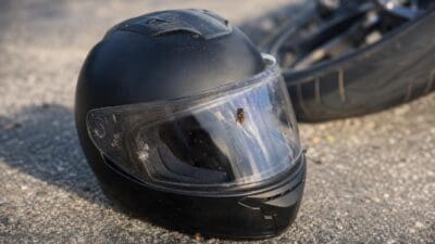Schwarzer Motorradhelm mit Wespe hinter dem Visier liegt auf dem Asphalt