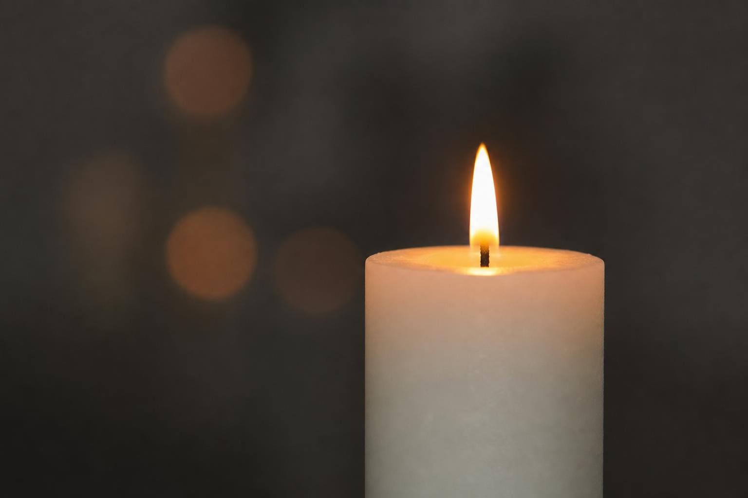 Brennende weiße Kerze mit warmer Flamme vor unscharfem dunklem Hintergrund