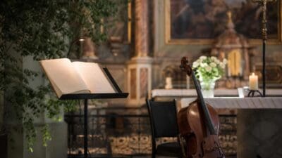 Ein aufgeschlagenes Buch liegt auf einem mit Lampe beleuchteten Lesepult, daneben ein Cello in einer Kirche.