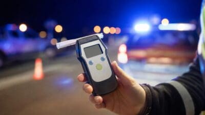 Hand eines Polizisten hält ein Alkoholmessgerät bei nächtlicher Verkehrskontrolle