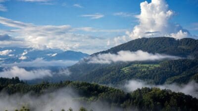 Bewaldete Berge in Kärnten mit Nebelbänken in den Tälern unter blauem Himmel