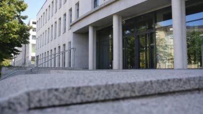 Eingang eines hellen Gerichtsgebäudes mit großen Säulen und Glasfassade sowie Steinstufen im Vordergrund