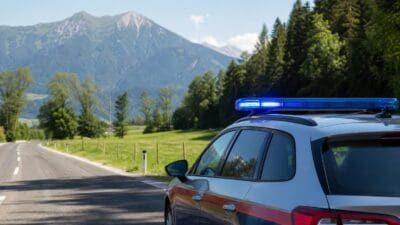 Polizeifahrzeug mit eingeschaltetem Blaulicht auf einer Landstraße vor Bergpanorama