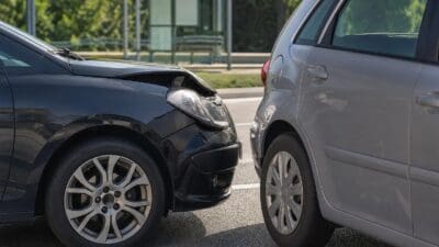 Schwarzer und grauer Pkw mit Frontschäden nach Kollision auf einer Straße vor einer Bushaltestelle