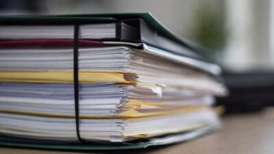 Nahaufnahme eines Stapels von Akten mit gelben Registerkarten und Gummiband auf einem Tisch