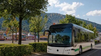 Weißer Bus mit grünem Streifen vor Jahrmarkt mit Riesenrad und Bergen