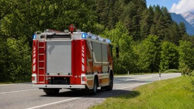 Heck eines roten Feuerwehrfahrzeugs mit Blaulicht auf einer Landstraße vor Bergen und Wald