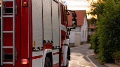 Rotes und weißes Feuerwehrfahrzeug parkt auf einer Straße in einem Wohngebiet bei Dämmerung.