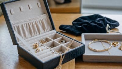 Offenes schwarzes Schmuckkästchen mit goldenen Ringen Perlen und Ketten auf einem Holztisch neben einem weiteren Schmuckbehälter