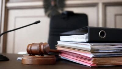 Richterhammer liegt neben bunten Aktenordnern auf einem Tisch im Gerichtssaal