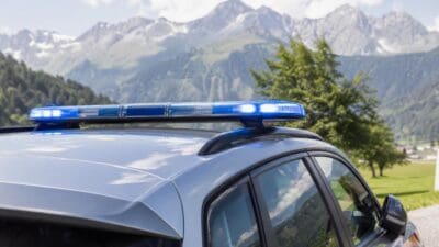 Aktiviertes blaues Blaulicht auf dem Dach eines grauen Polizeifahrzeugs vor einer Bergkulisse.