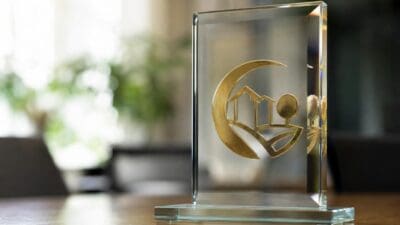 Transparenter Glaspreis mit goldenem Emblem aus Mond und Häusern auf Holztisch