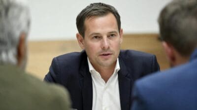 Max Lercher im dunklen Anzug spricht an einem Tisch mit zwei Männern